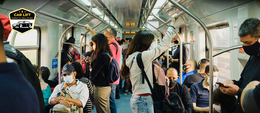 Crowded interior of a metro train with seated and standing passengers, most wearing face masks, during daytime. The scene reflects public transport usage with a diverse group of commuters holding onto handrails or using mobile phones. cheap car lift Dubai to Abu Dhabi